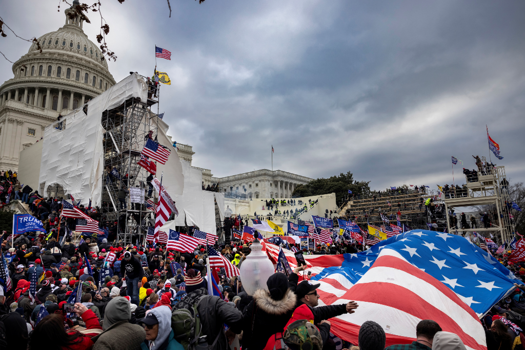 Trump supporters storm the U.S. Capitol on January 6, 2021. They cover the stairs and the bleachers set up for the inauguration. They carry American flags, Trump flags, anti-Semitic flags, and other white supremacist flags.